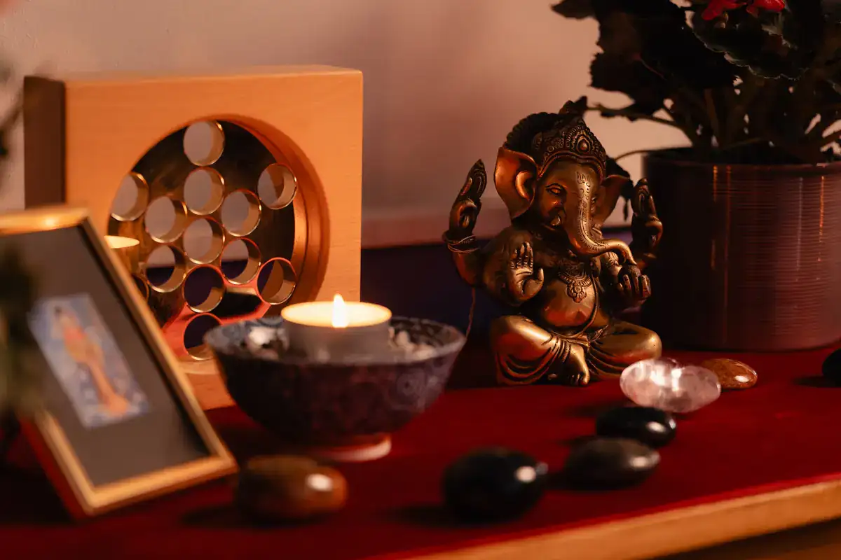 Détail d'un autel de soin au cabinet Koram à Yverdon-les-Bains : statue de Ganesh en bronze, bougie allumée, galets de massage, cristaux de roche et cadre photo sur une étagère rouge