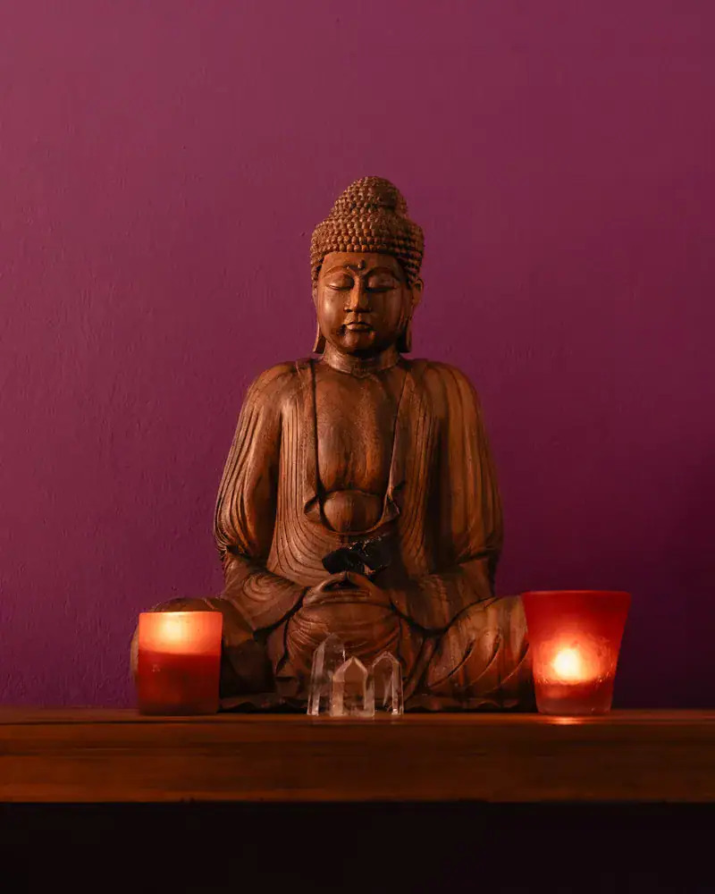 Statue de Bouddha en bois et bougies dans la salle du cabinet Koram à Yverdon-les-Bains. Ambiance calme pour séances de kinésiologie et massage.