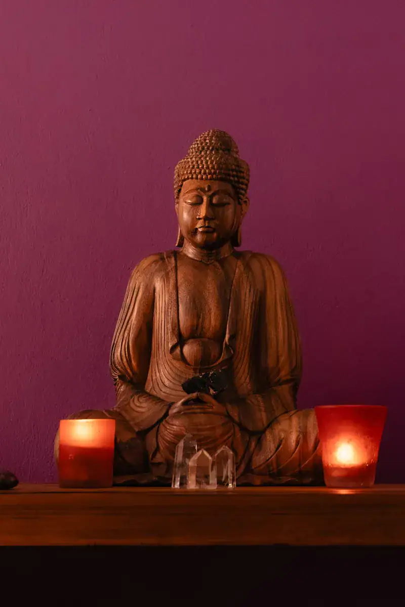 Statue de Bouddha en bois avec bougies et cristaux dans l'espace détente du cabinet Koram à Yverdon-les-Bains. Ambiance propice au lâcher-prise pour les séances de massage avec approche viscérale.