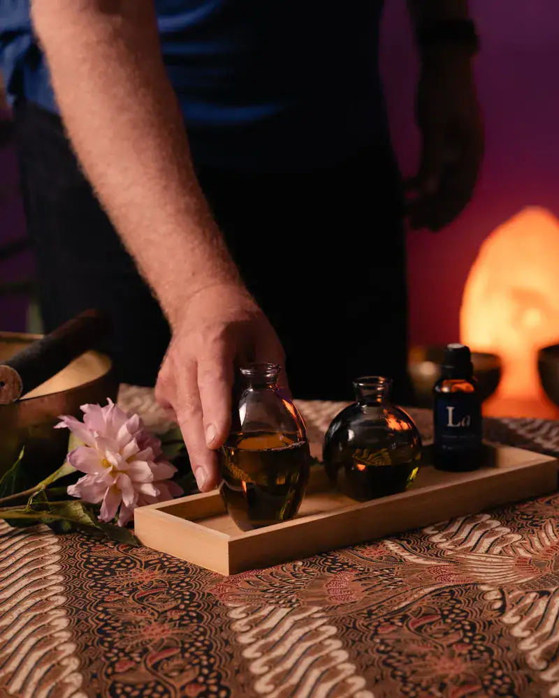 Préparation des huiles de massage par Stéphane Maillefer au cabinet Koram à Yverdon-les-Bains. Huiles naturelles et fleurs sur une table de massage professionnelle.