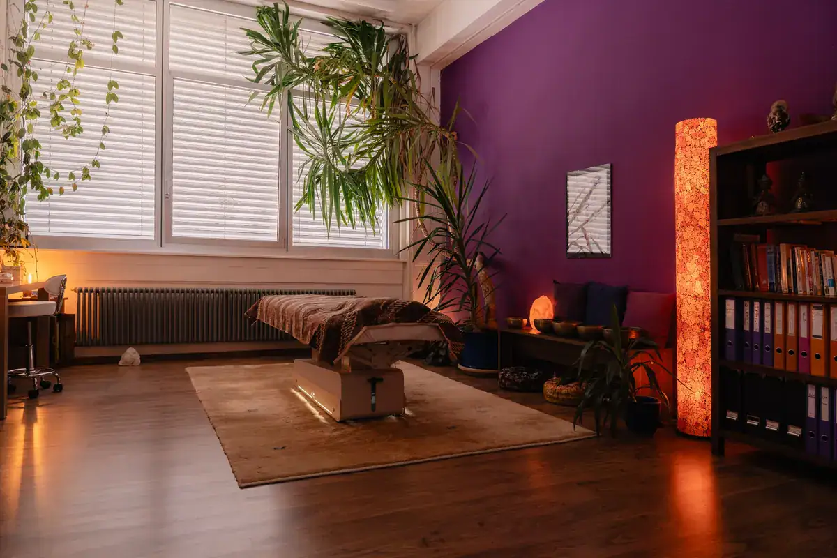 Vue d'ensemble du cabinet Koram à Yverdon-les-Bains. Espace de soin lumineux avec table de massage, plantes et ambiance chaleureuse pour séances de kinésiologie et massage avec Stéphane Maillefer.